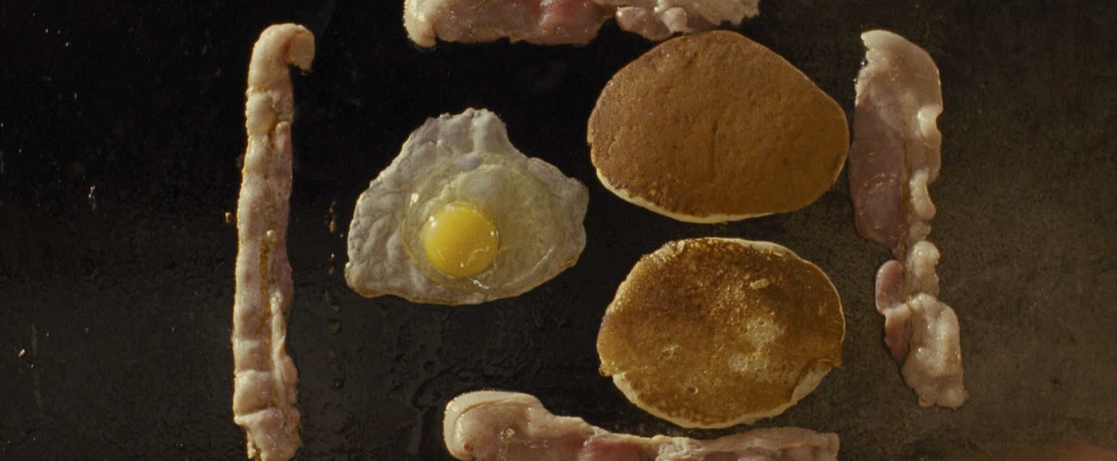 bacon, eggs, and sausages are being cooked on a grill