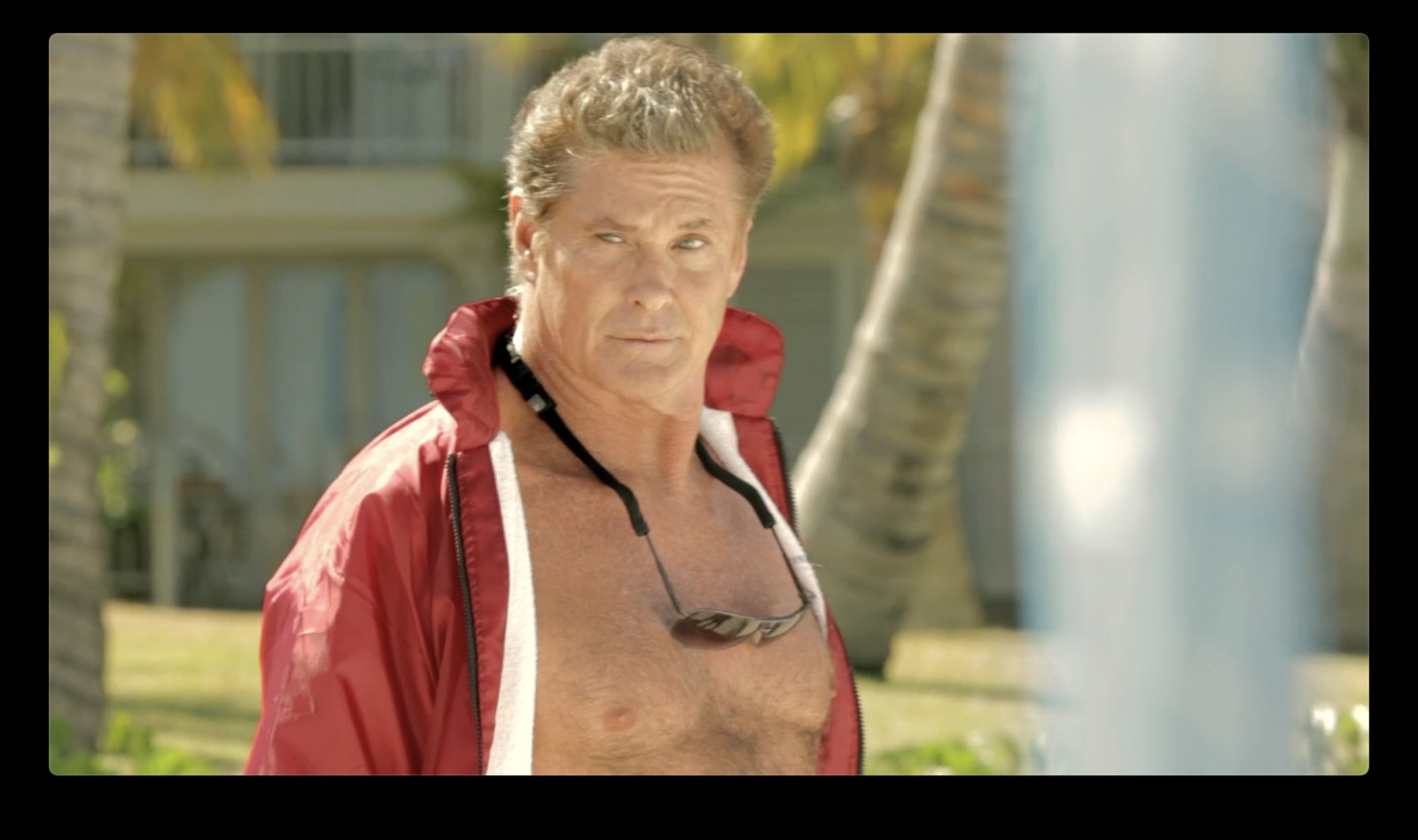 a man in a red jacket standing next to a palm tree