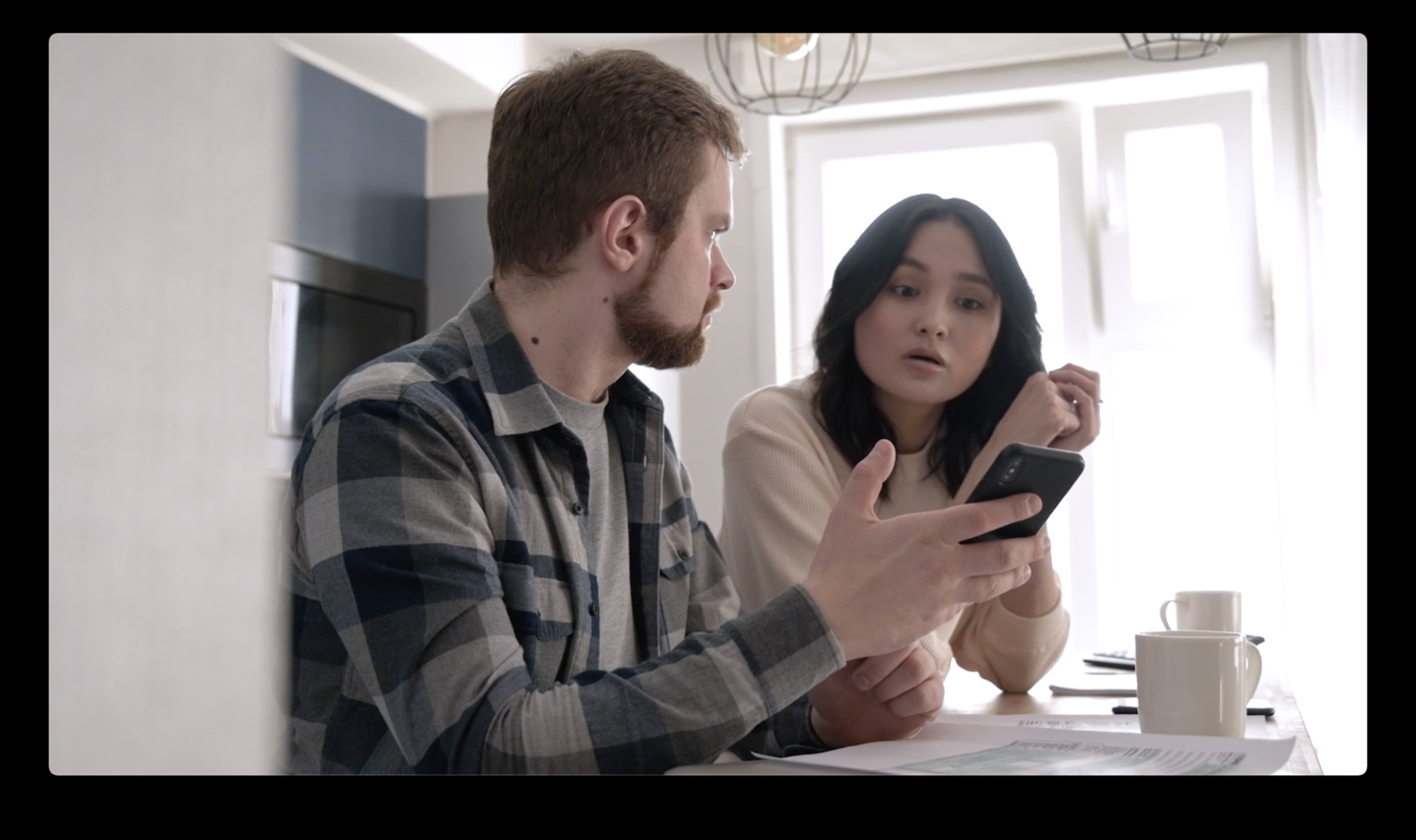 a man and a woman sitting at a table looking at a cell phone