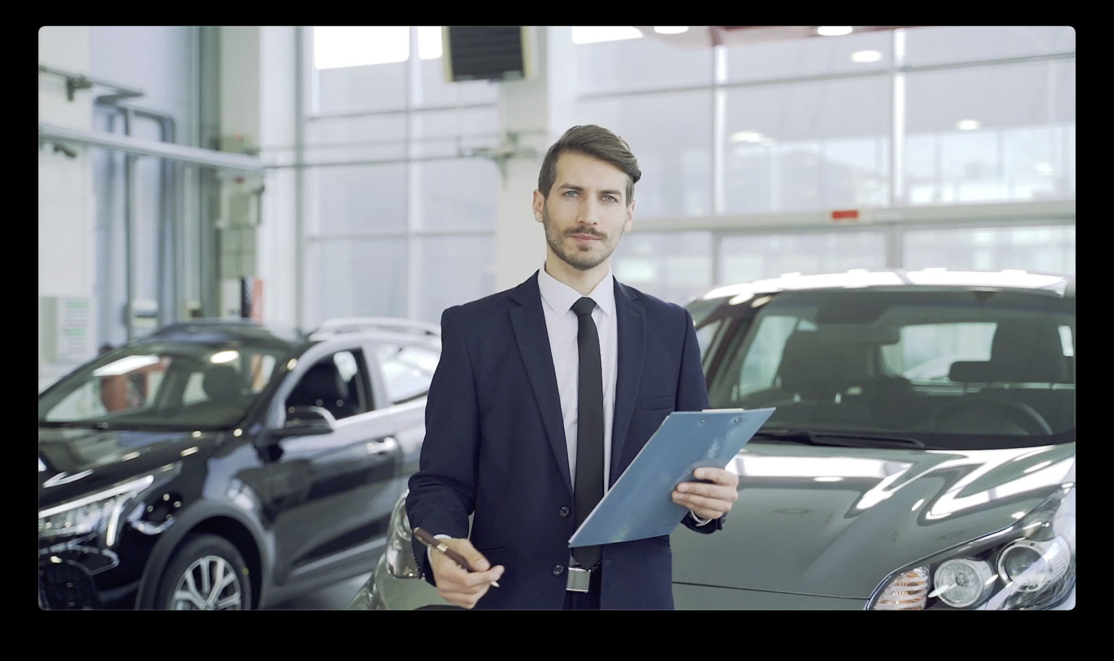 a man in a suit holding a clipboard in front of a car