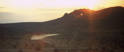 a plane flying over a dirt road near a mountain