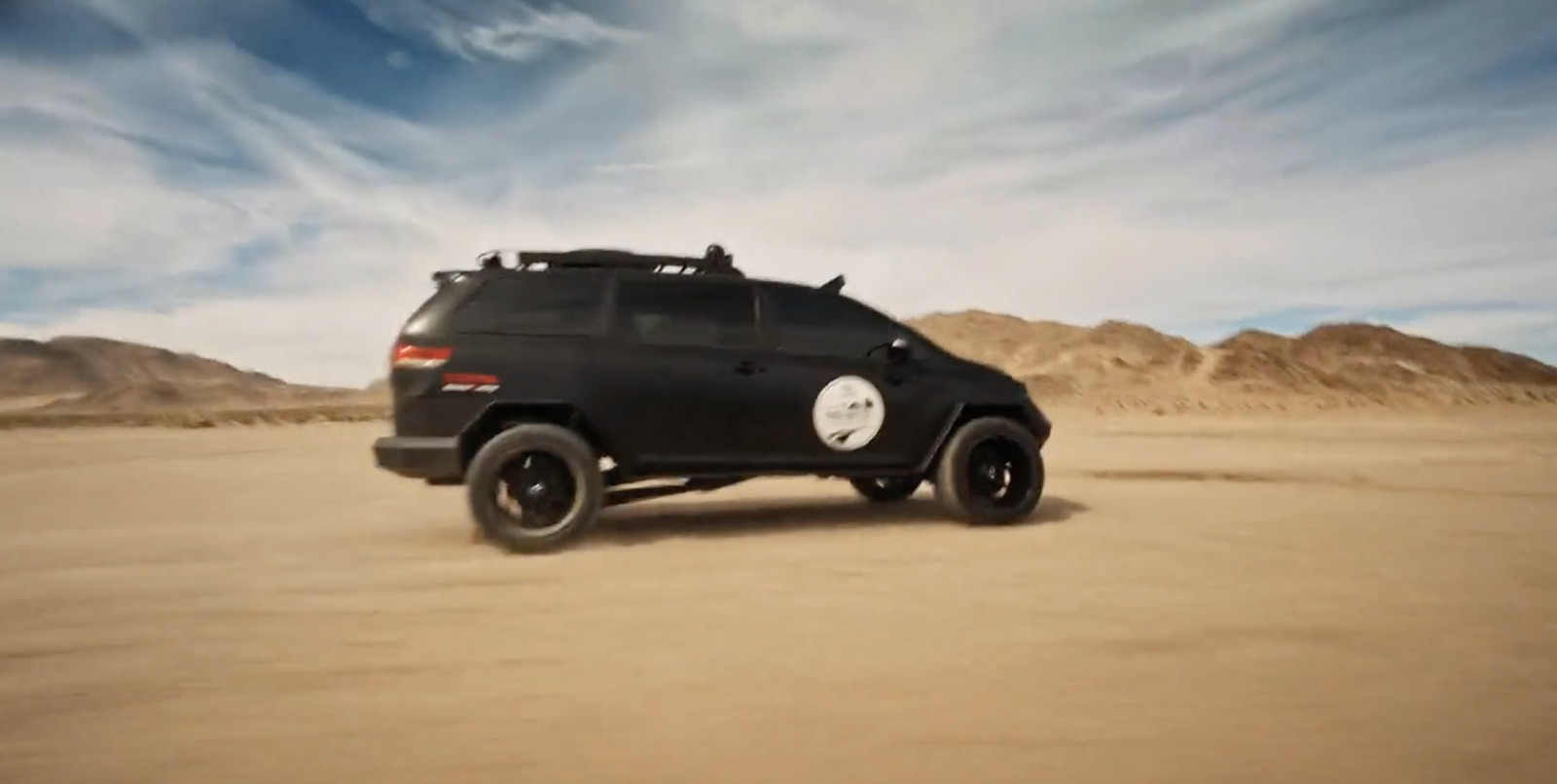 a black suv driving through a desert with mountains in the background