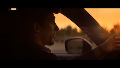 a man driving a car with the sun setting in the background