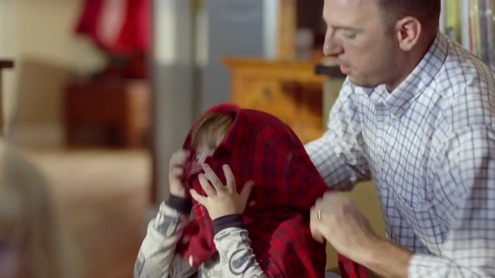 a man helping a little girl put on a plaid shirt