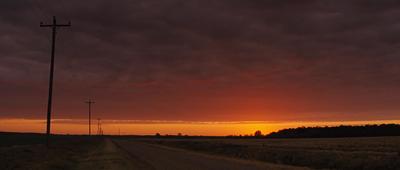 the sun is setting over a rural road