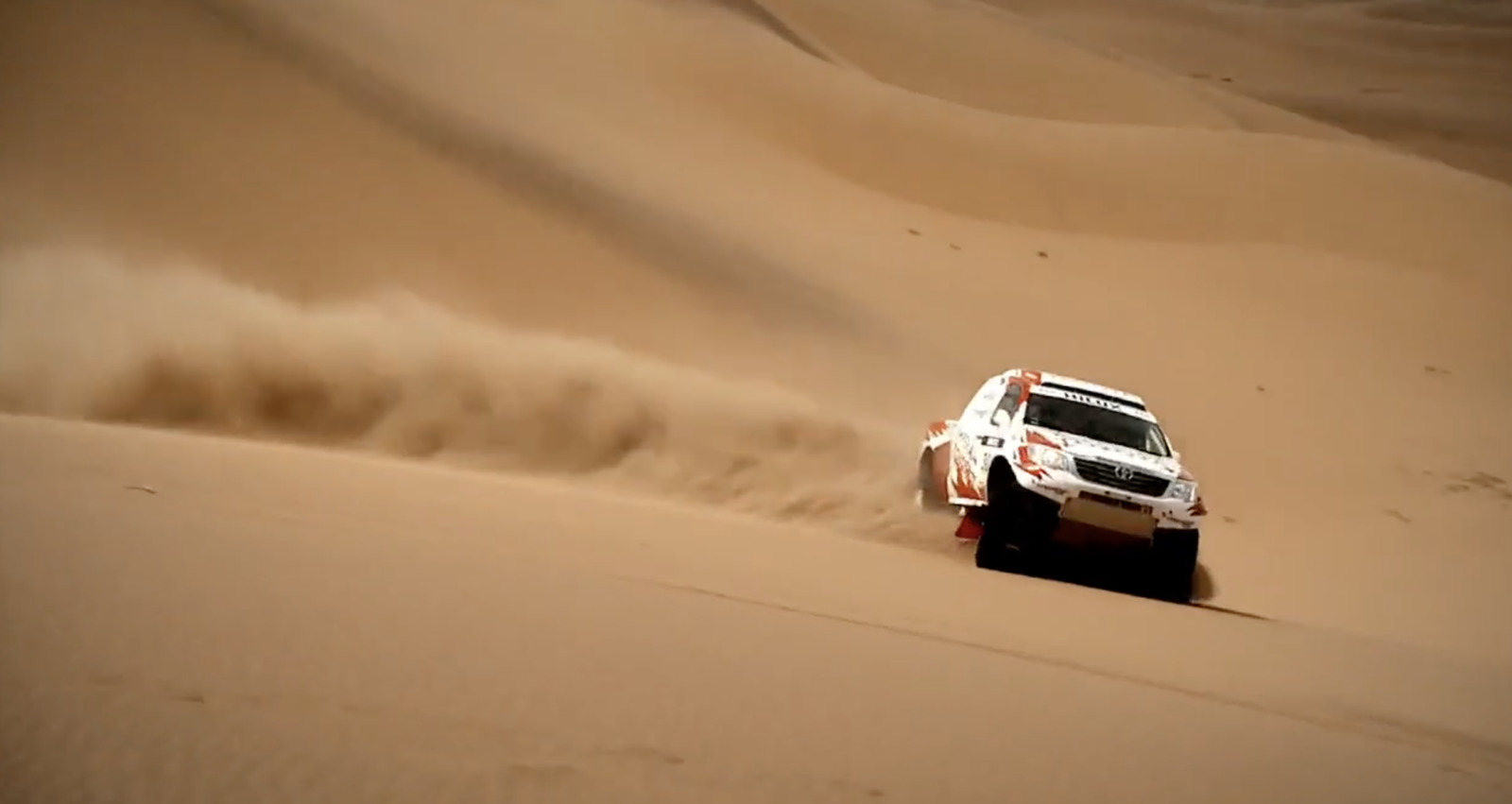 a white truck driving through a desert filled with sand