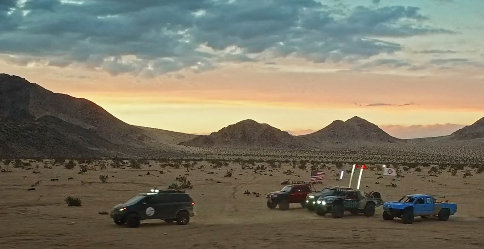 a group of four trucks driving through a desert