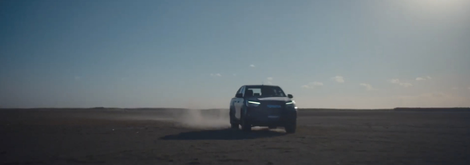 a car driving down a dirt road under a blue sky