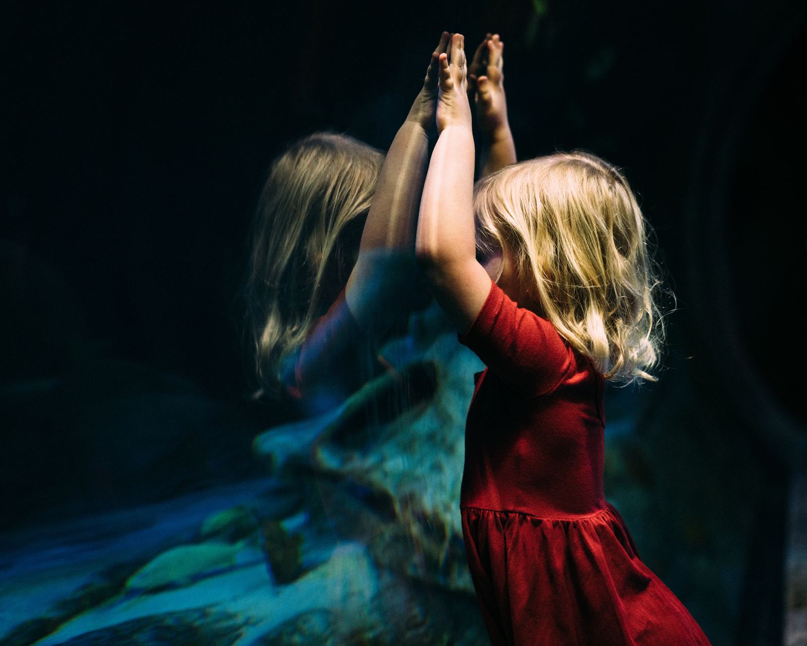 a little girl in a red dress reaching for something