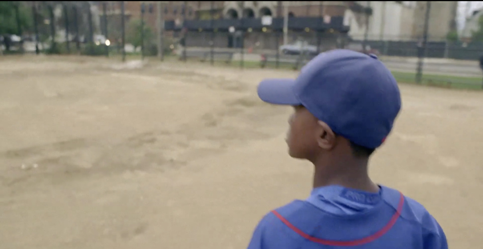 a young boy in a blue baseball uniform standing on a baseball field