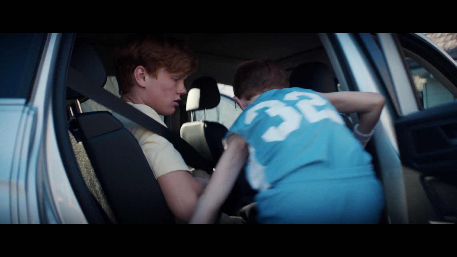 two boys sitting in a car talking to each other