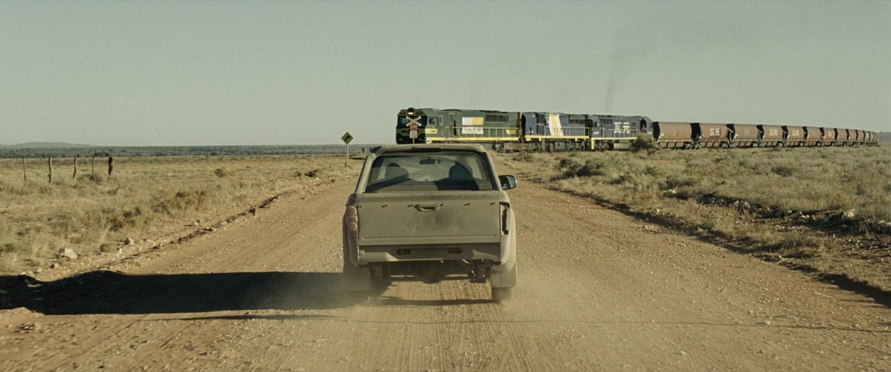 a truck driving down a dirt road next to a train