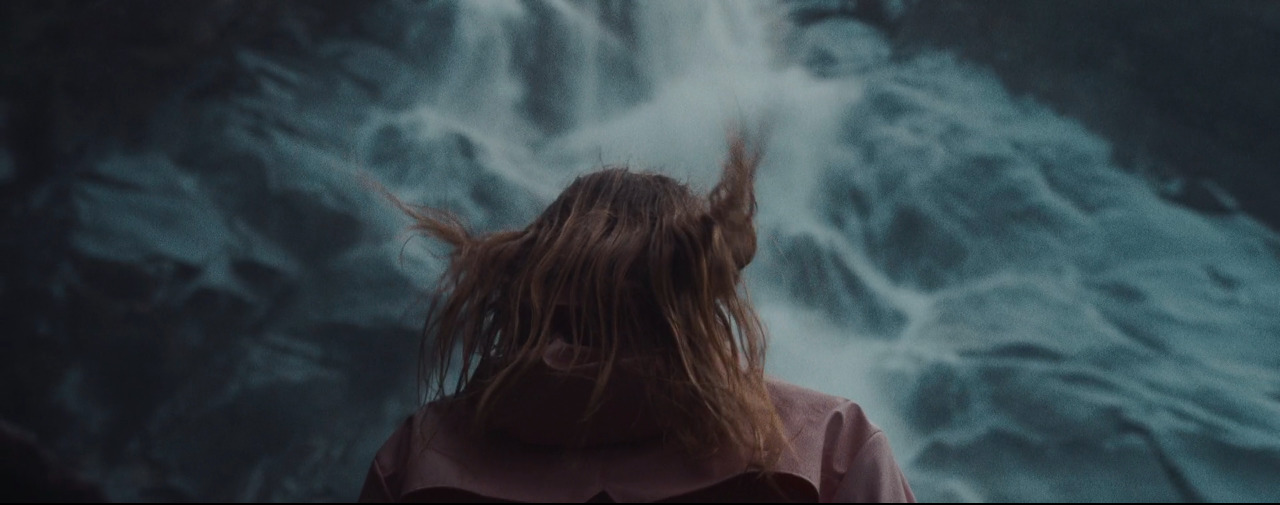 a woman with long hair standing in front of a waterfall