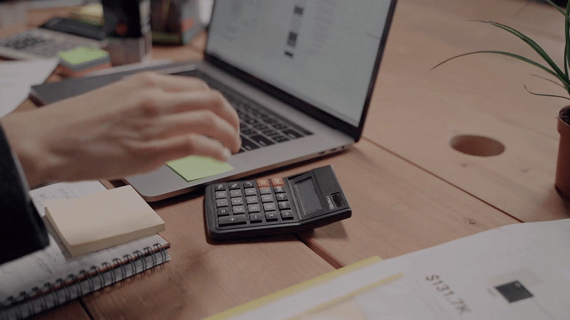 a person typing on a calculator next to a laptop