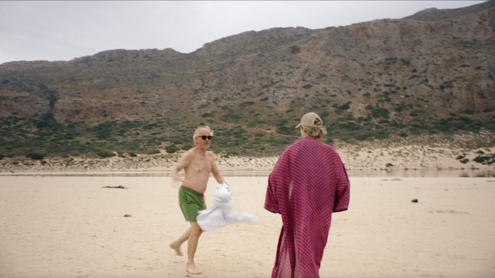 a couple of men walking across a sandy beach