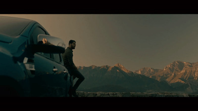 a man standing next to a blue car in front of mountains