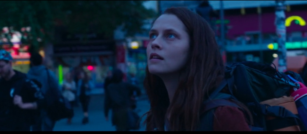 a woman with long hair and a backpack looks off into the distance