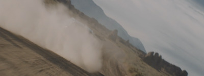 a car driving down a dirt road next to a mountain