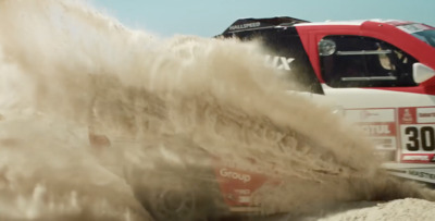 a truck driving down a sandy road next to a red truck