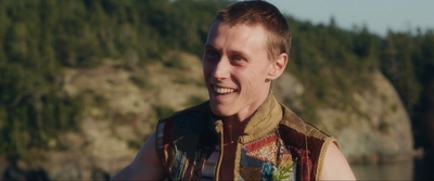 a man wearing a colorful vest standing in front of a body of water