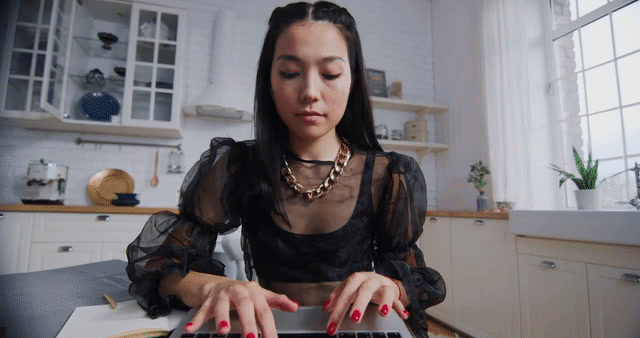 a woman sitting at a kitchen table typing on a laptop