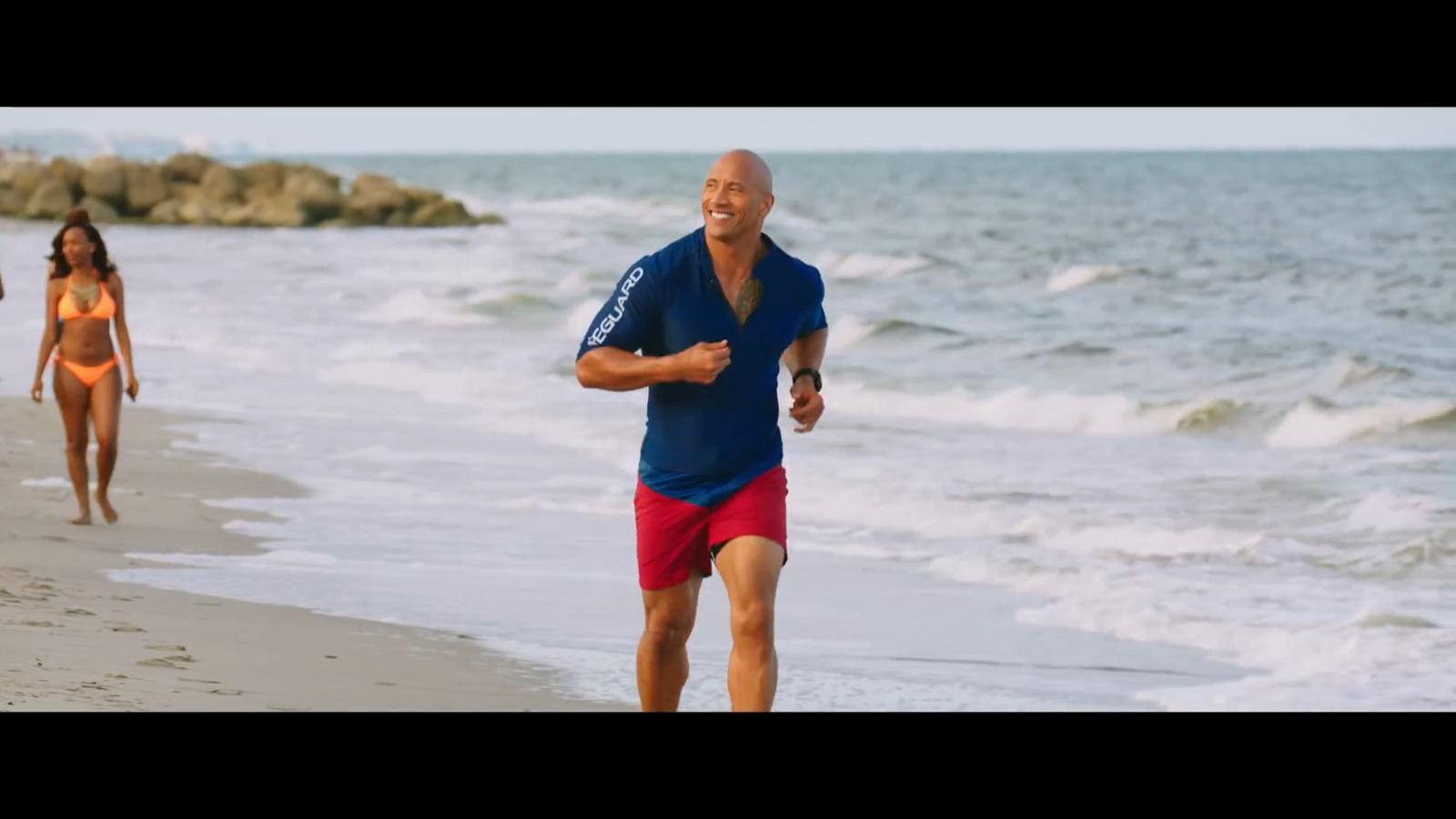 a man running on the beach with a woman in the background