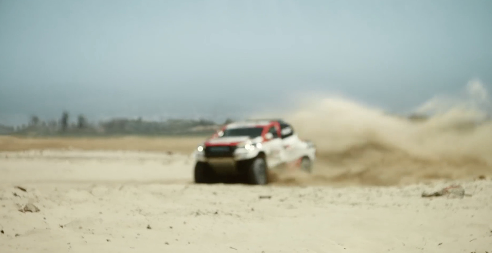 a white truck driving through a sandy field