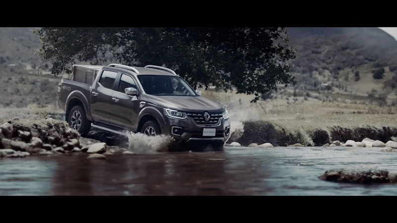 a grey truck driving through a river next to a forest