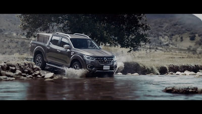 a grey truck driving through a river next to a forest