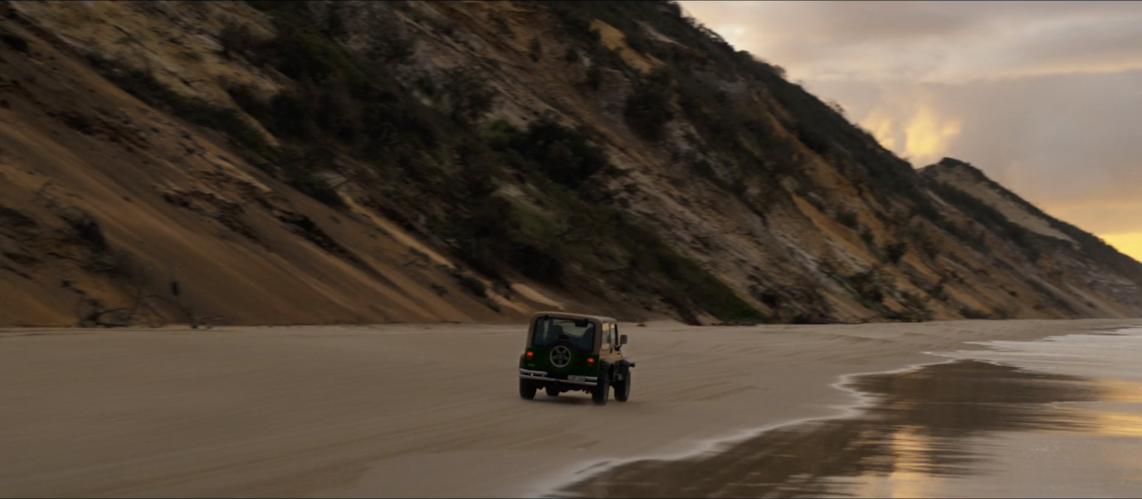 a jeep driving down a beach next to a cliff