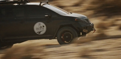 a black car driving down a dirt road