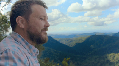 a man with a beard standing in front of mountains