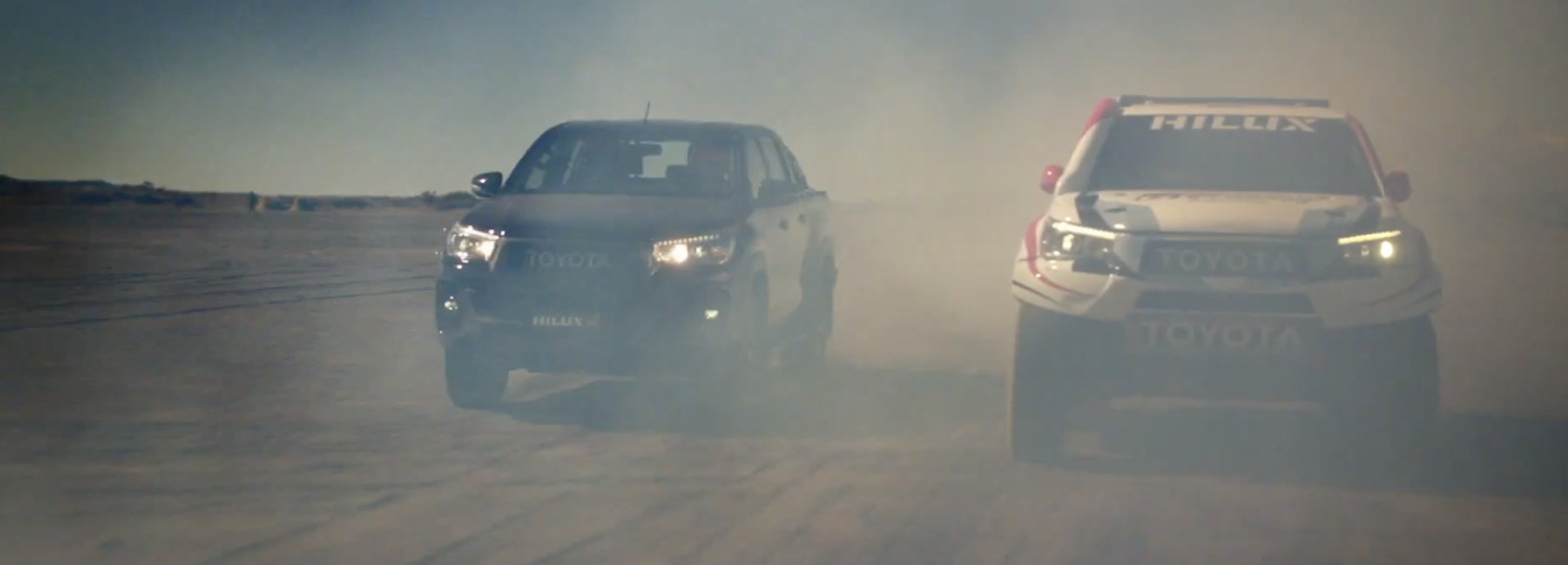 two trucks driving down a dirt road next to each other