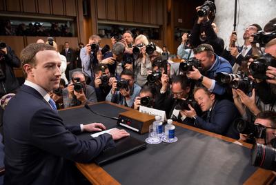 a man sitting at a table surrounded by photographers