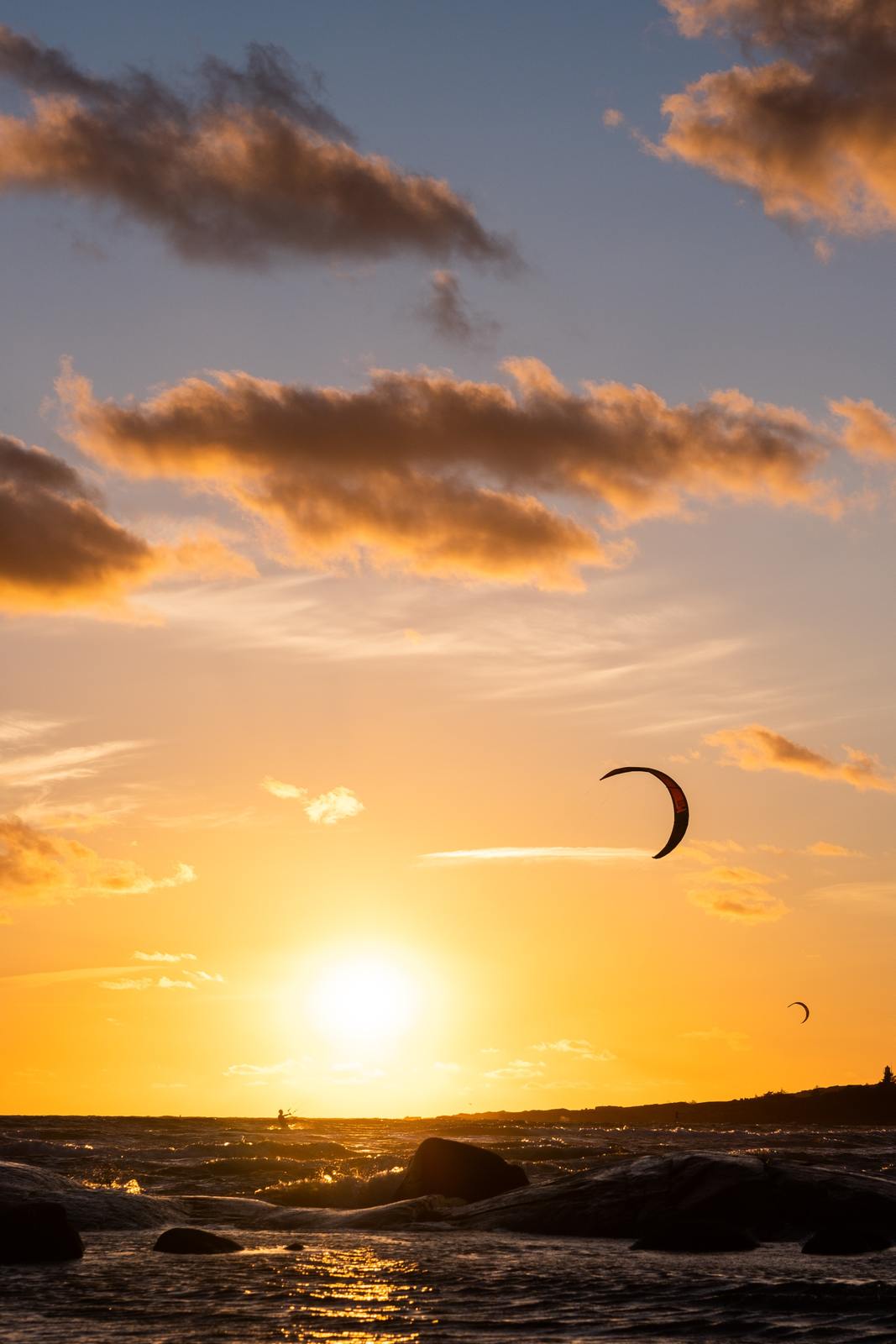 the sun is setting over the ocean with a kite flying in the sky