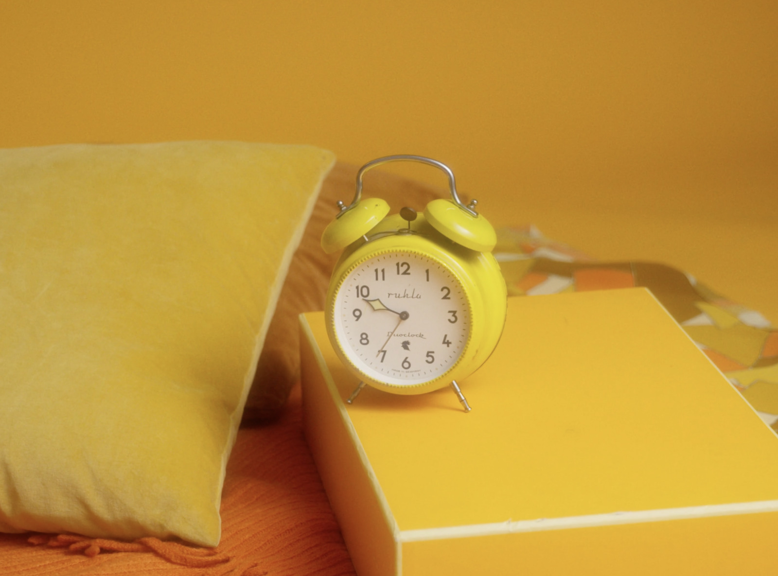 a yellow alarm clock sitting on top of a yellow pillow