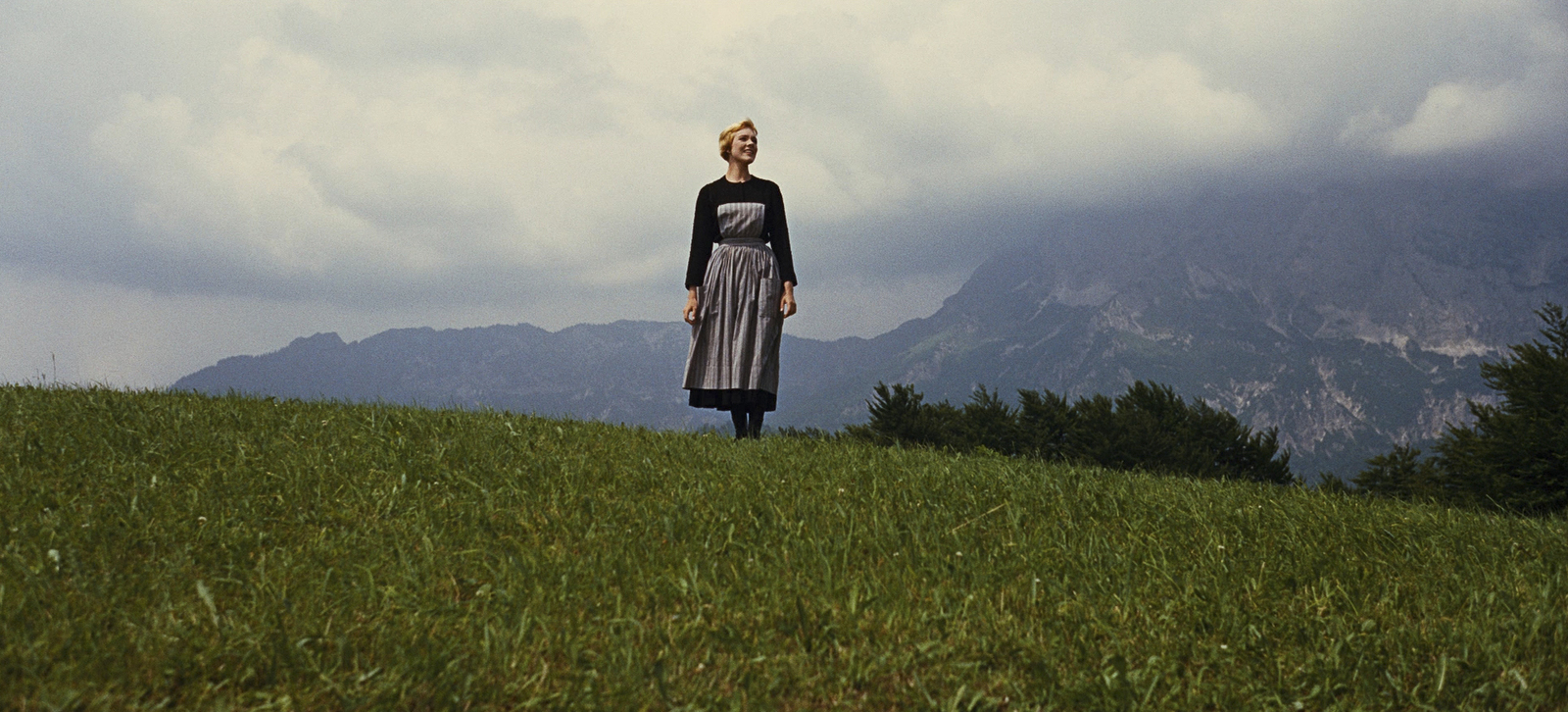 a woman standing on top of a lush green hillside