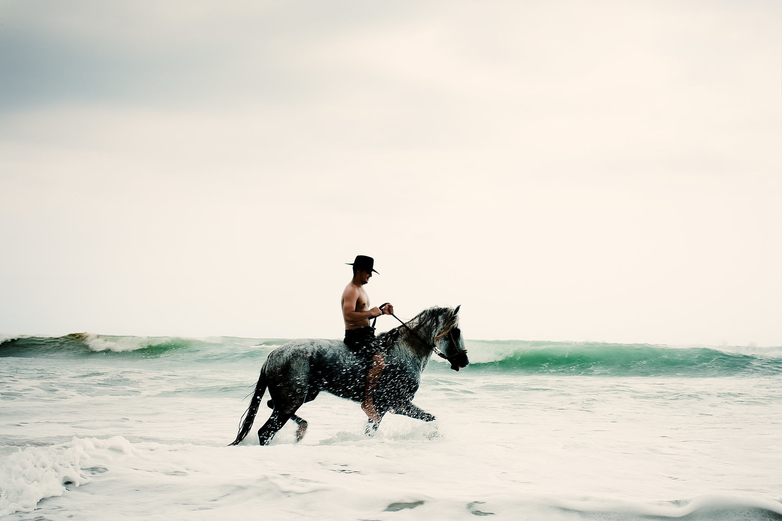 a man riding on the back of a horse through the ocean