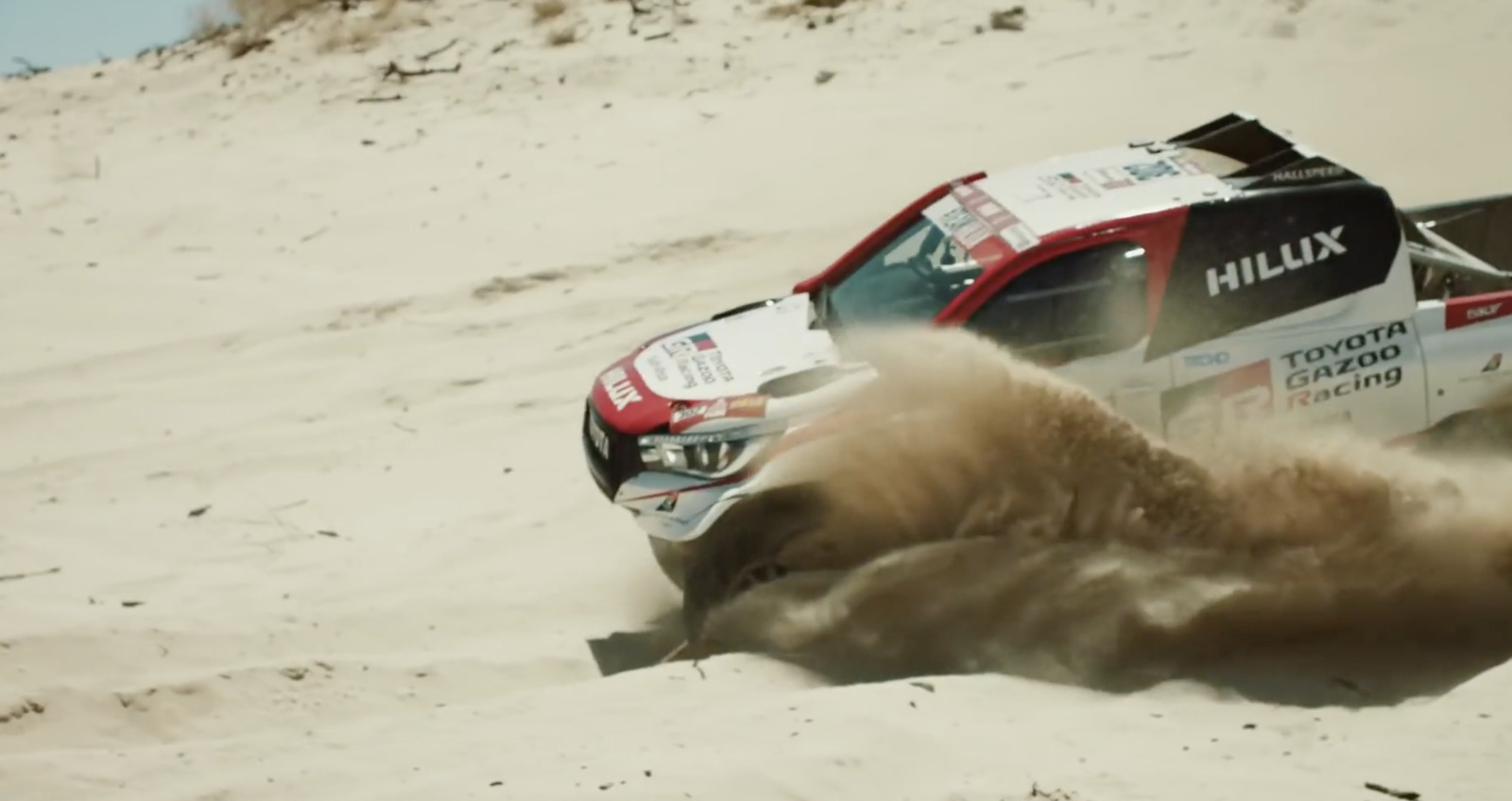 a red and white truck driving on top of a sandy hill