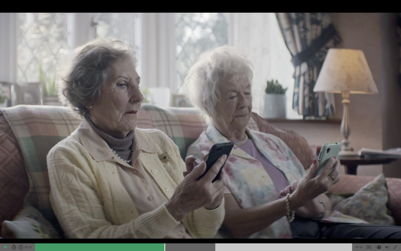 two older women sitting on a couch looking at a cell phone