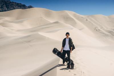 a man standing in the sand with a skateboard