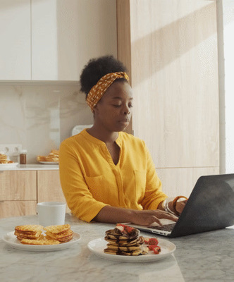 a woman sitting at a kitchen table using a laptop