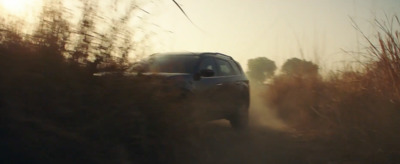 a car driving down a dirt road next to tall grass