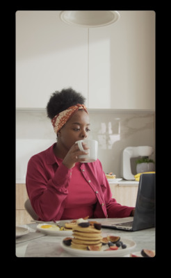 a woman sitting at a table with a laptop and a stack of pancakes