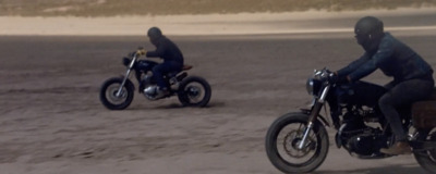 two people riding motorcycles on a sandy beach