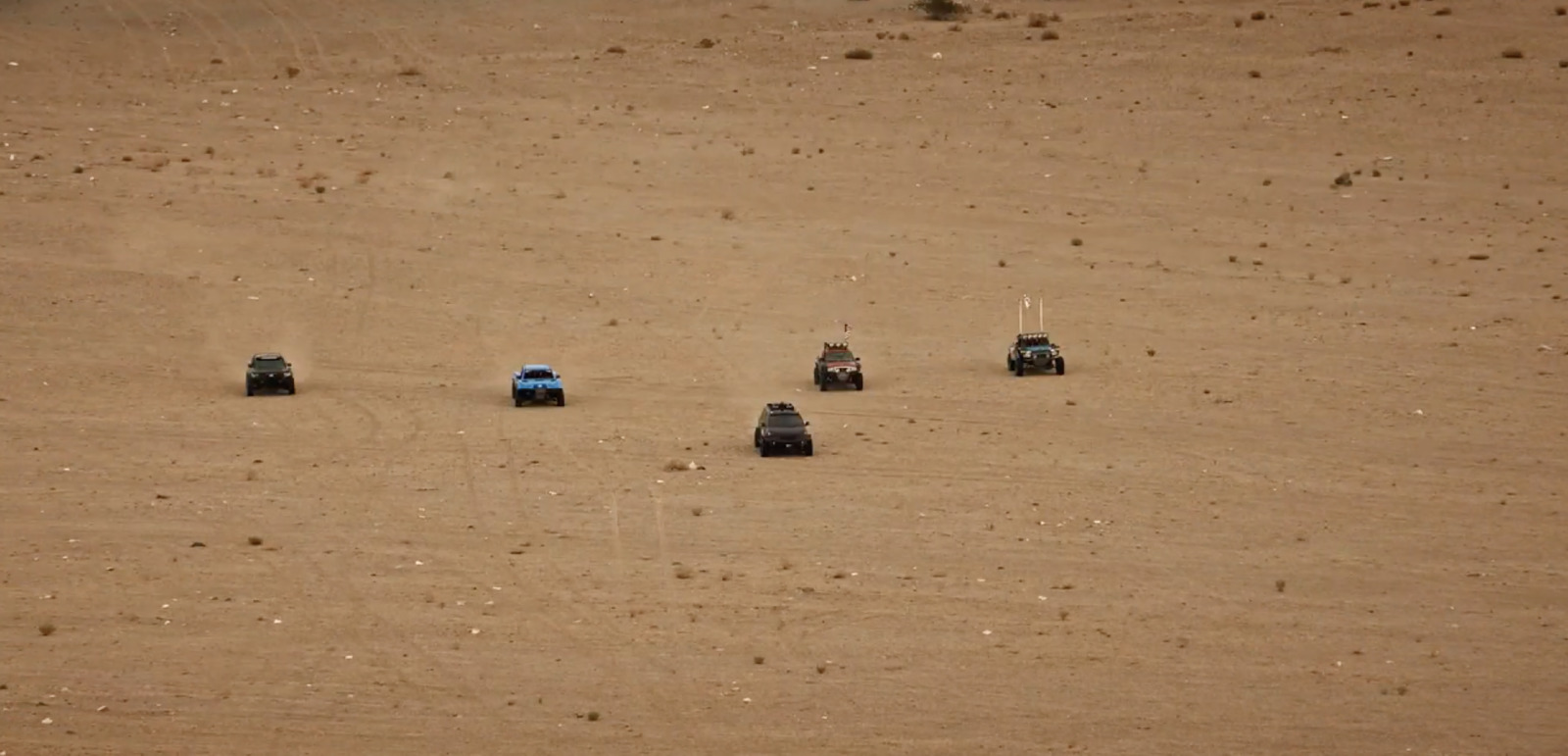 a group of four cars driving across a sandy field