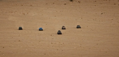 a group of four cars driving across a sandy field