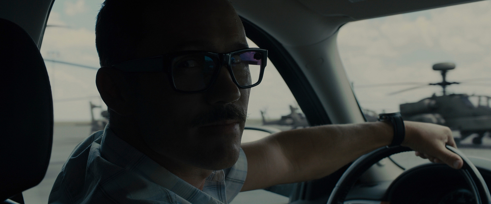 a man driving a car with a helicopter in the background