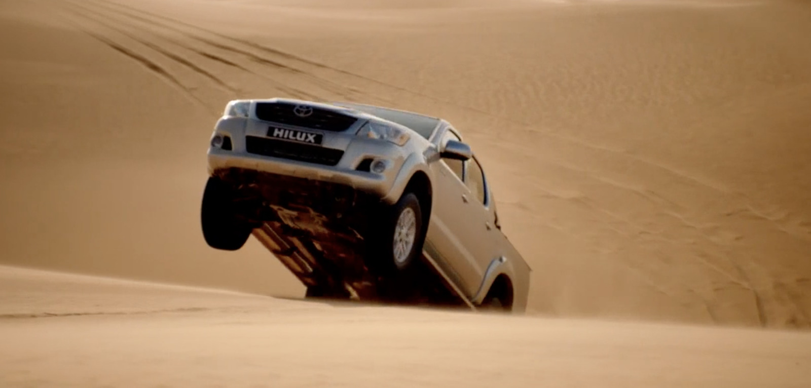 a white truck driving through a desert filled with sand