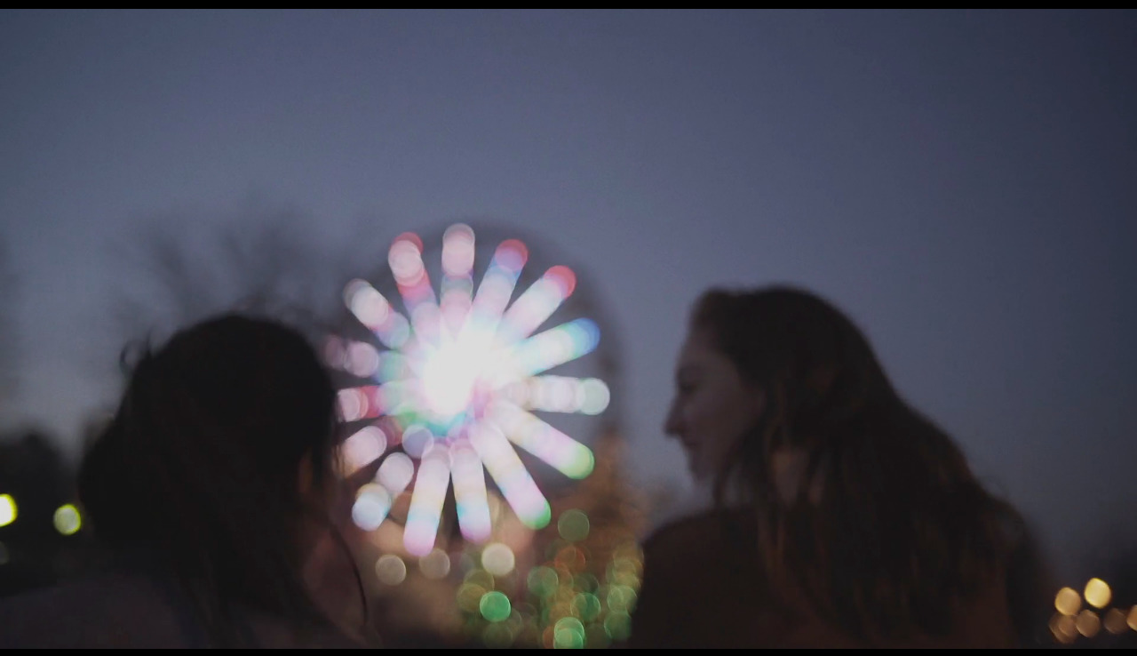 two women standing next to each other in front of a fireworks display